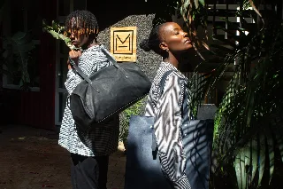 Two models outside the TUG workshop with a leather weekender and tote