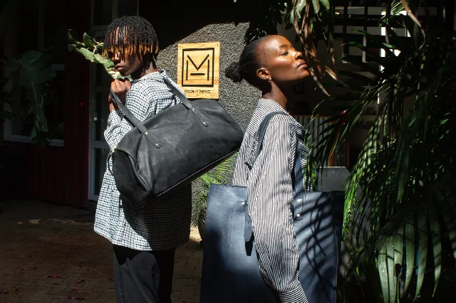 Two models outside the TUG workshop with a leather weekender and tote