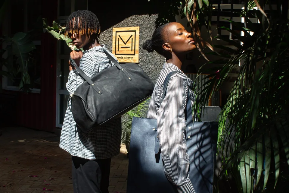 Two models outside the TUG workshop with a leather weekender and tote