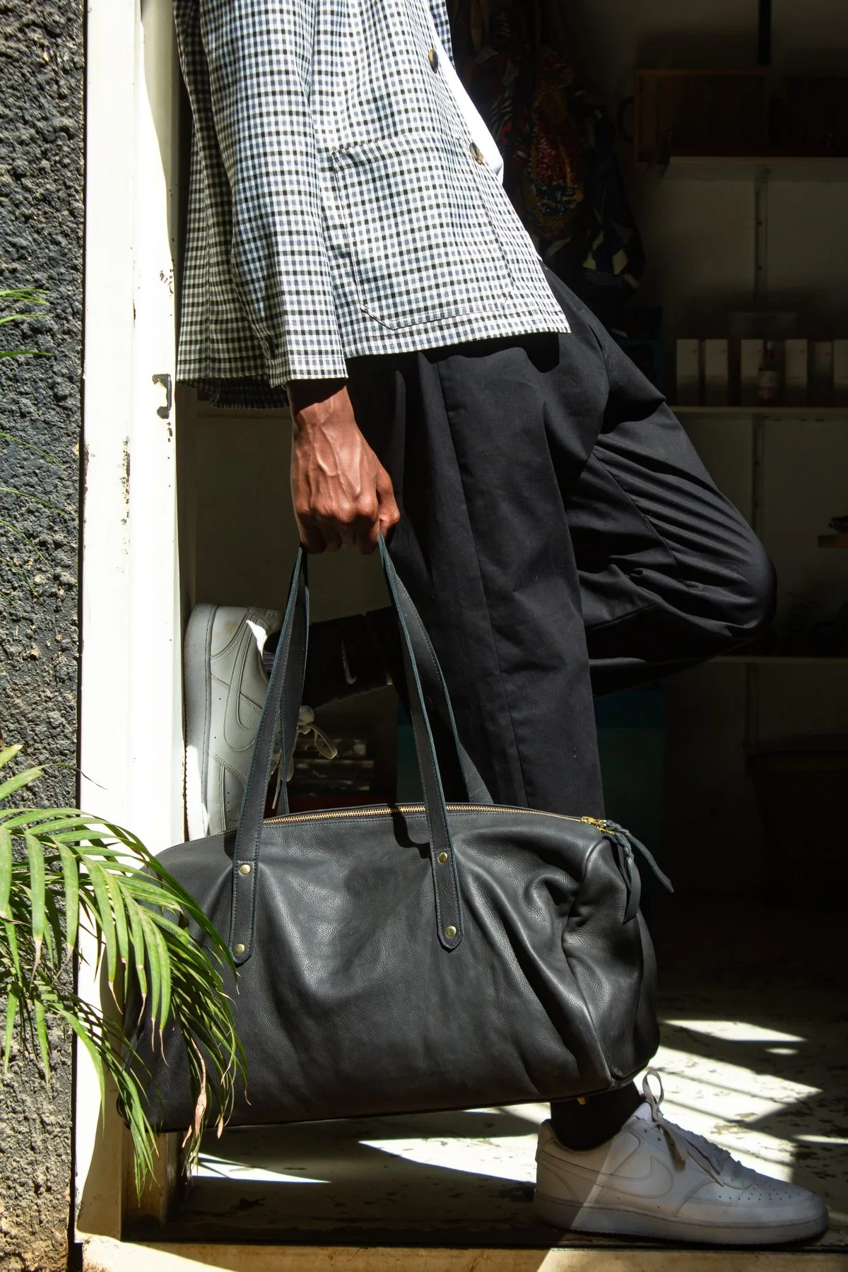 Black full-grain leather weekender bag held at the door
